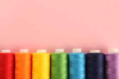 Different colorful sewing threads on pink background, flat lay. Space for text