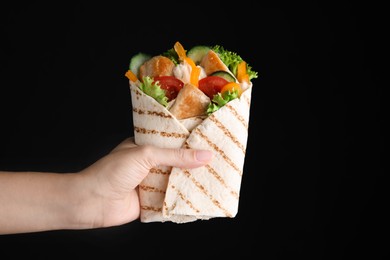 Woman holding delicious shawarmas with chicken meat and vegetables on black background, closeup