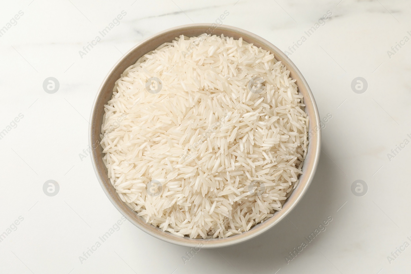 Photo of Raw basmati rice in bowl on white marble table, top view