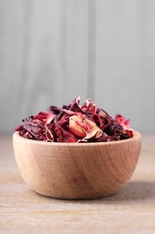 Photo of Dry hibiscus tea in bowl on wooden table, space for text