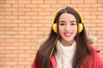 Photo of Beautiful young woman listening to music with headphones against brick wall. Space for text