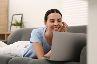 Photo of Happy woman working with laptop on sofa at home