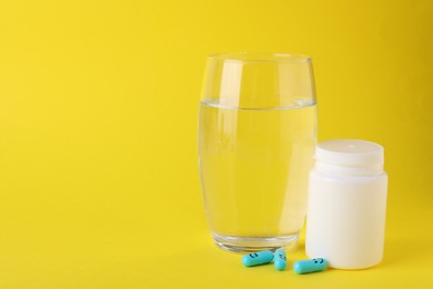 Photo of Antidepressants with happy emoticons, medical jar and glass of water on yellow background, space for text