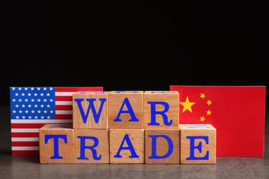 Photo of Words War Trade made of wooden cubes, American and Chinese flags on grey table against black background