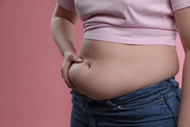 Woman touching belly fat on pink background, closeup. Overweight problem