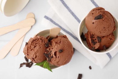 Photo of Paper cups with tasty chocolate ice cream on white tiled table, flat lay