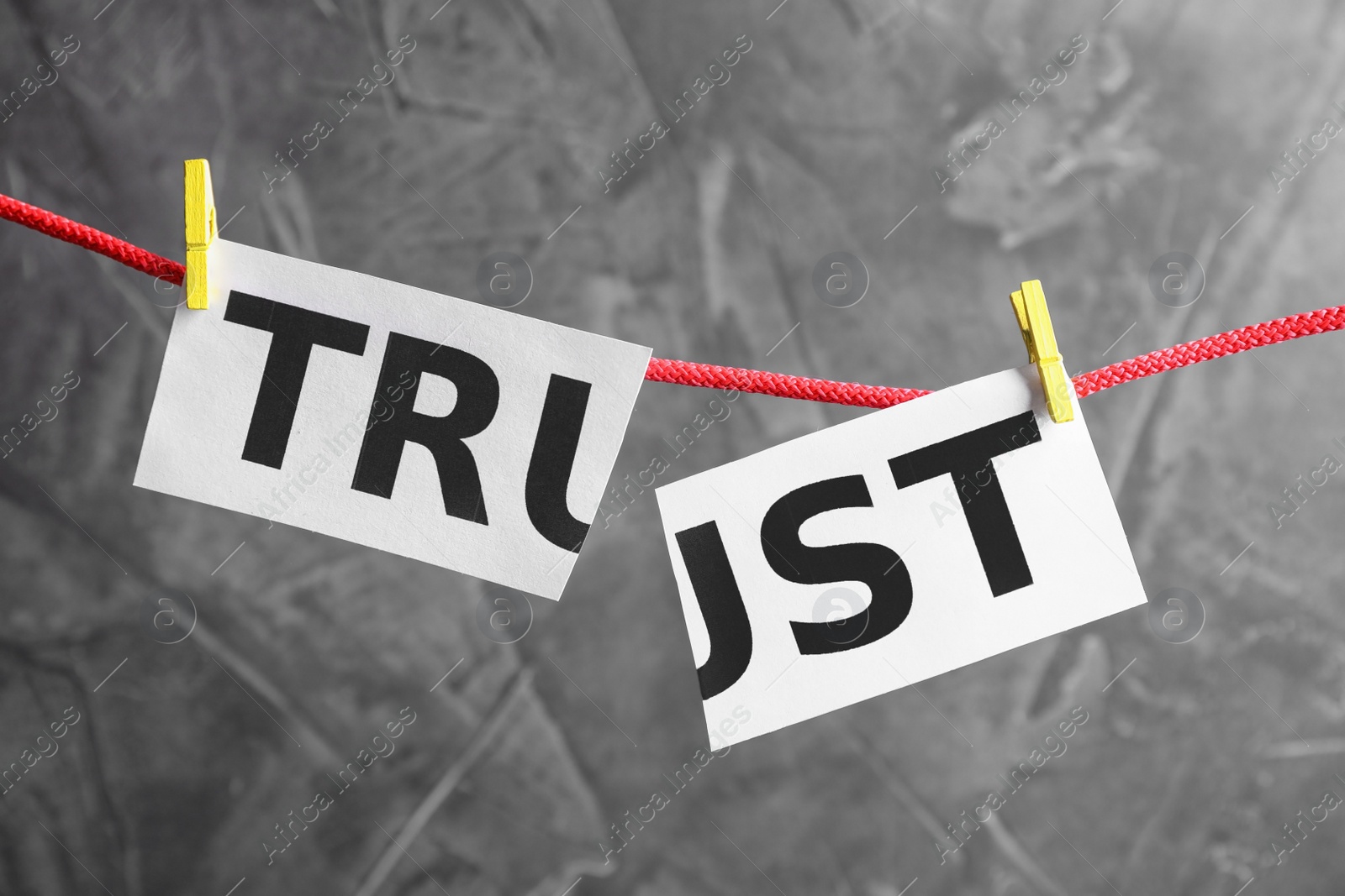Photo of Cut word TRUST hanging on rope against grey background. Concept of jealousy