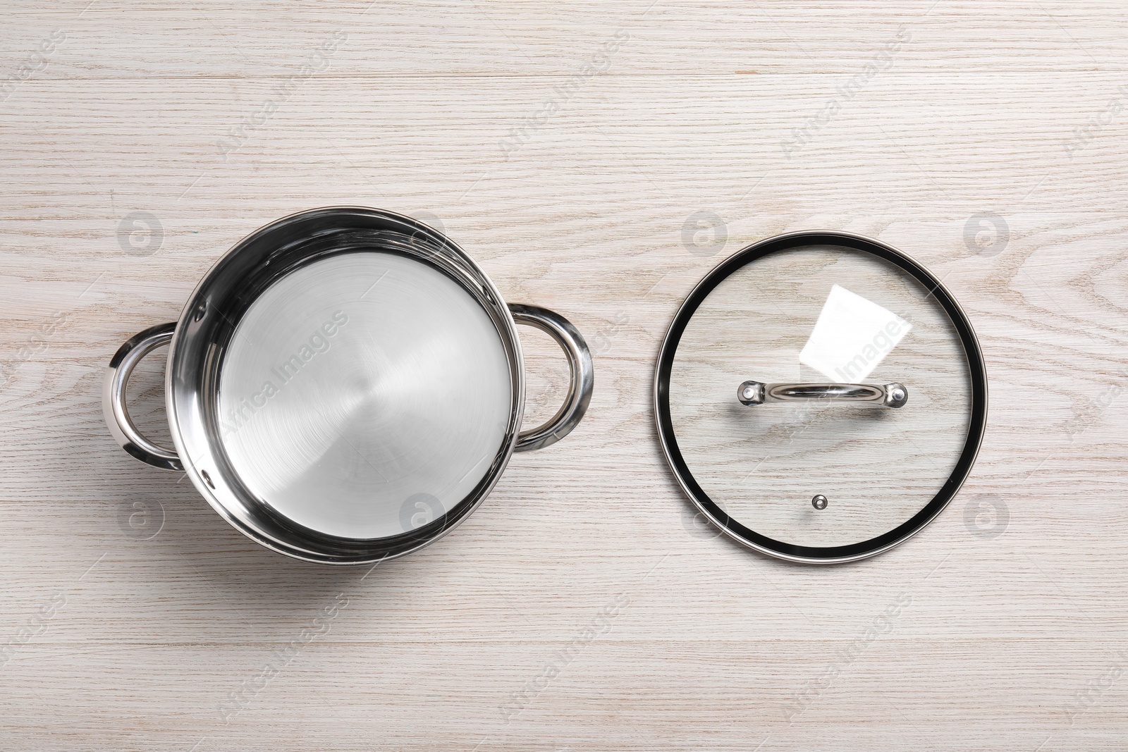Photo of Steel pot and glass lid on white wooden table, flat lay