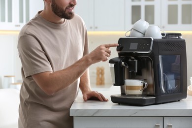 Young man preparing fresh aromatic coffee with modern machine in kitchen, closeup