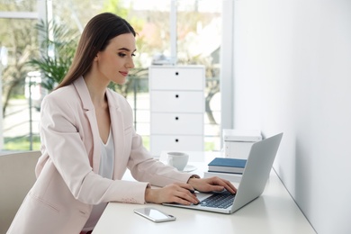 Young businesswoman using laptop at table in office