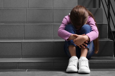 Photo of Child abuse. Upset girl sitting on stairs, space for text