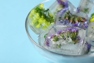 Photo of Bowl of ice cubes with flowers on blue background, closeup