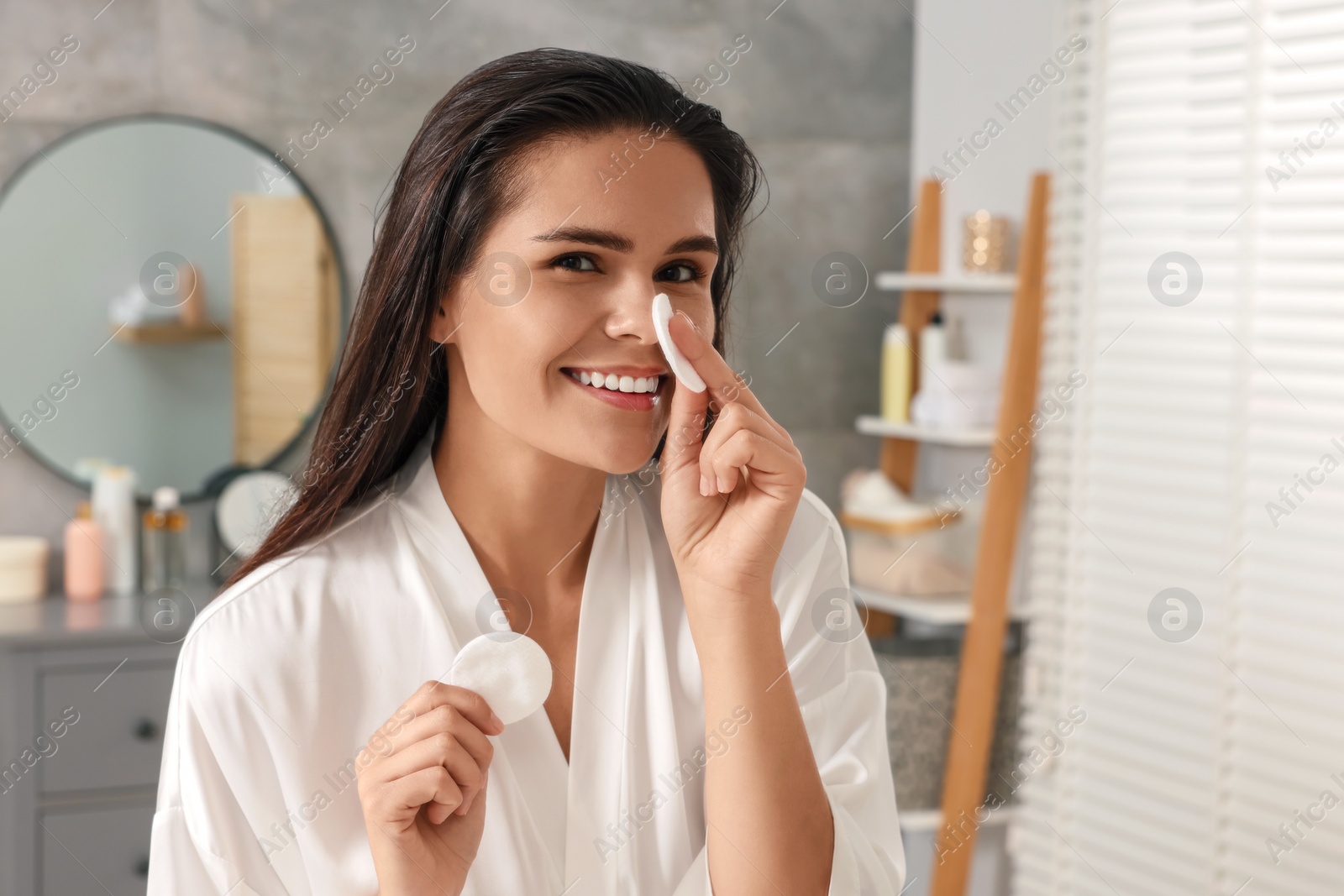 Photo of Young woman cleaning her face with cotton pads in bathroom