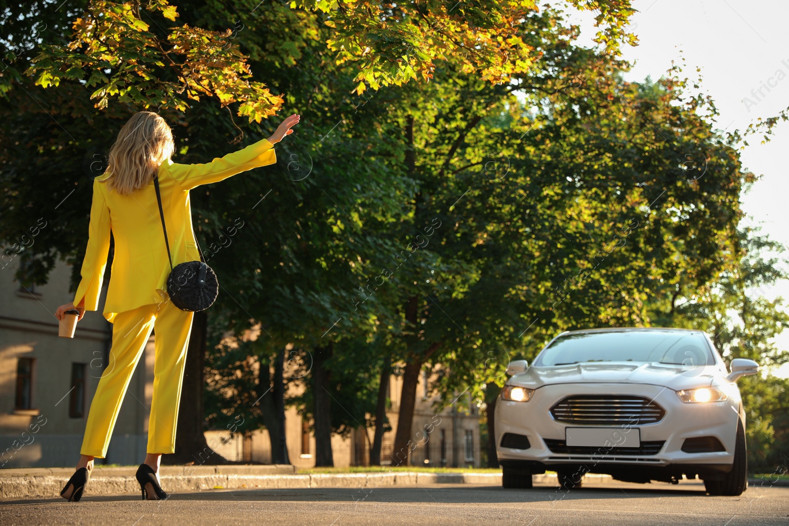 Photo of Young businesswoman catching taxi on city street, back view