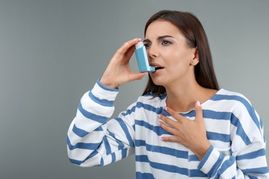 Photo of Young woman using asthma inhaler on color background
