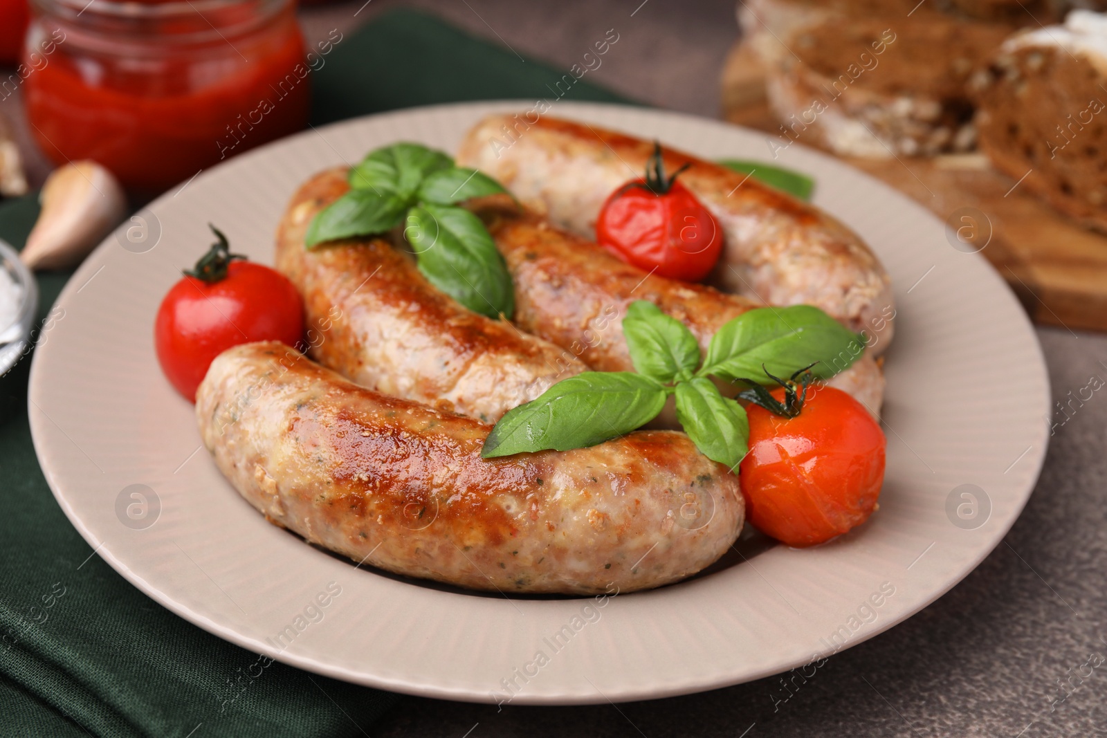 Photo of Plate with tasty homemade sausages, basil leaves and tomatoes on brown textured table, closeup