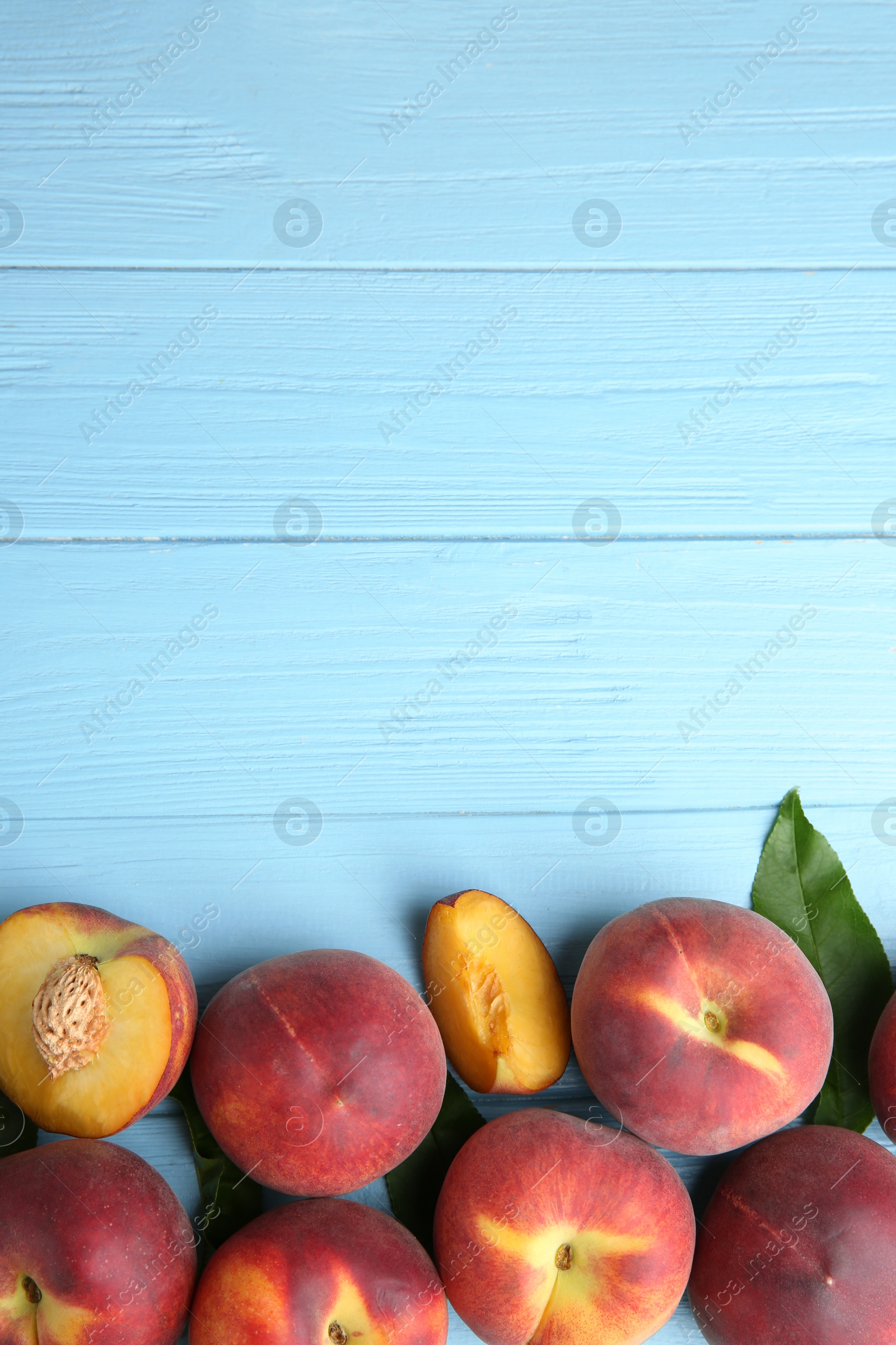 Photo of Fresh peaches and leaves on blue wooden table, top view with space for text