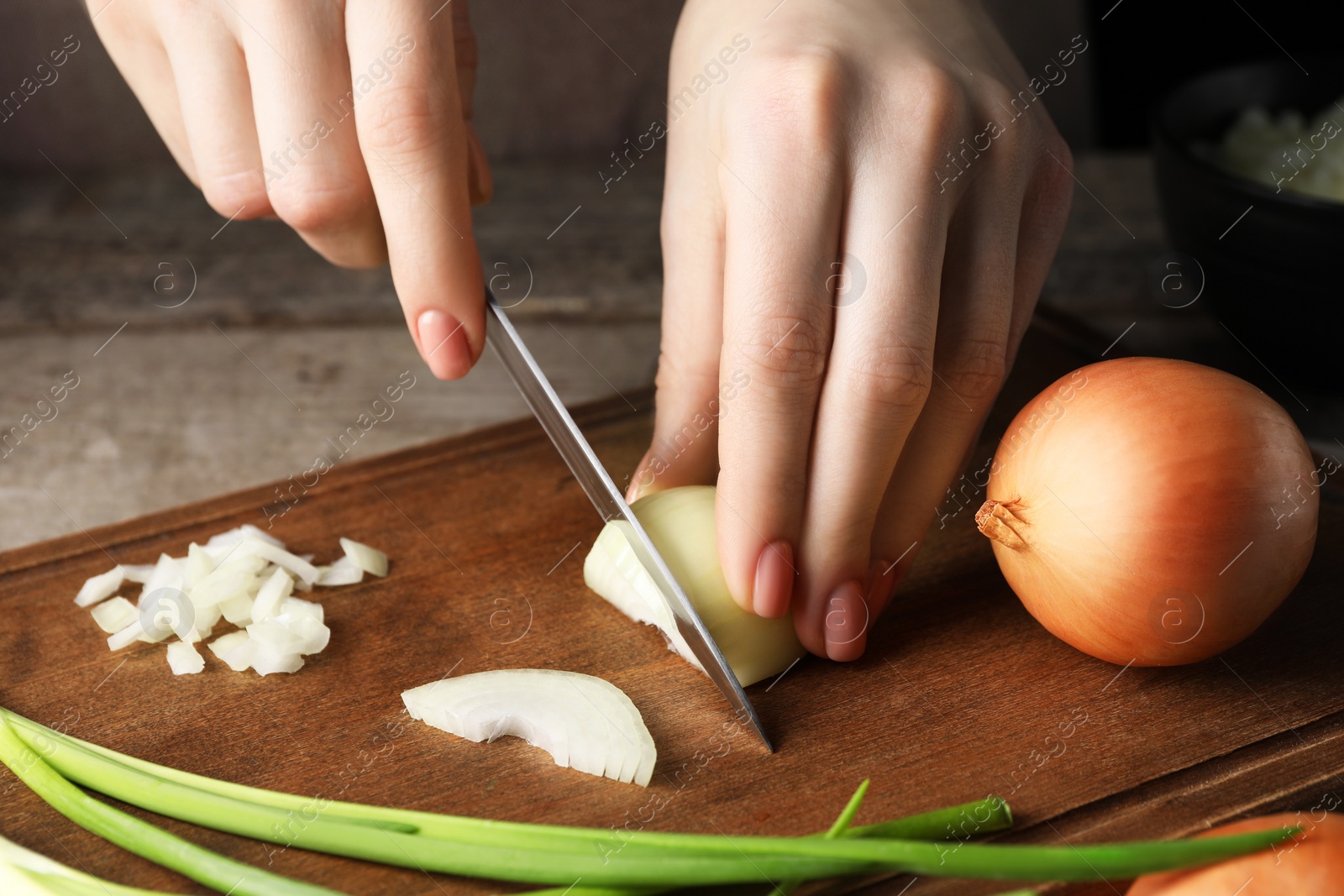 Photo of Woman cutting ripe onion at wooden table, closeup