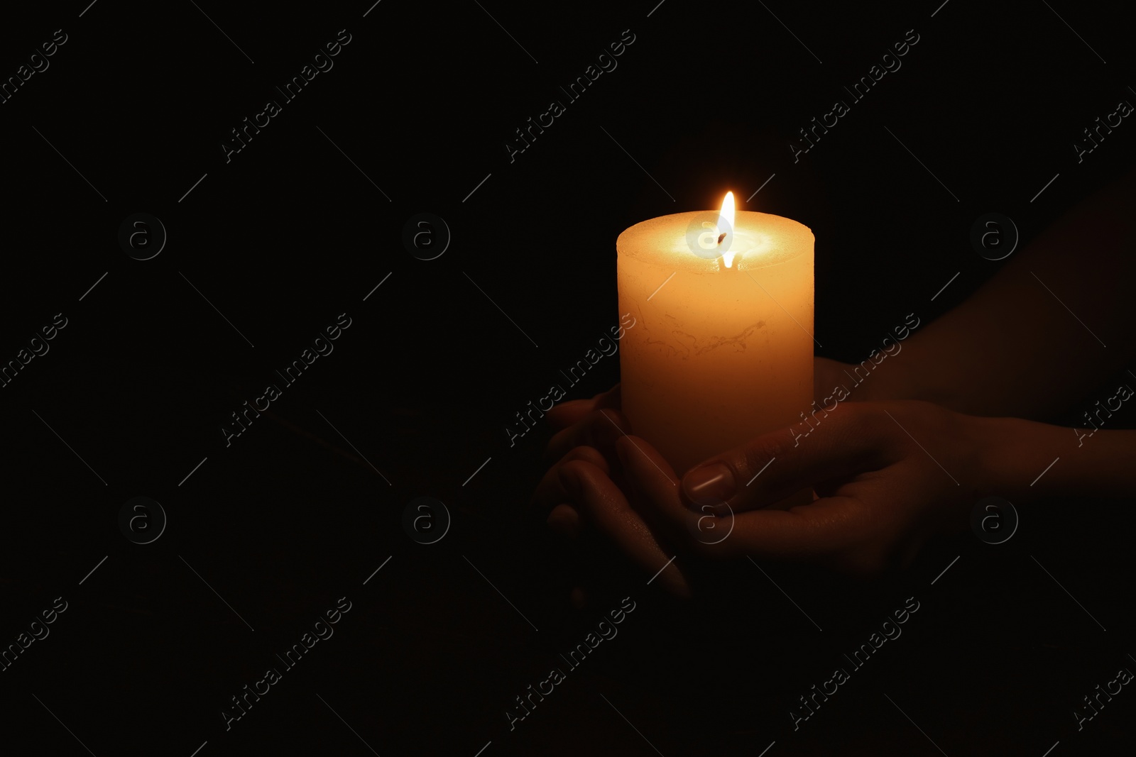 Photo of Woman holding burning candle in hands on black background, closeup. Space for text