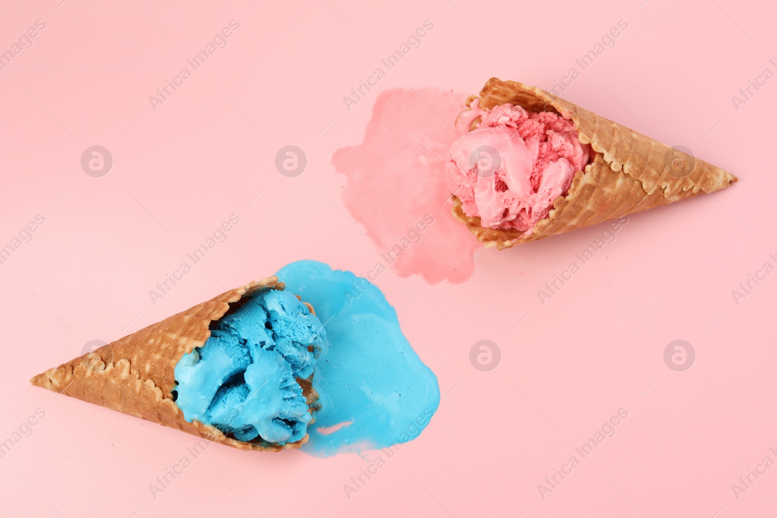 Photo of Melted ice cream in wafer cones on pink background, flat lay