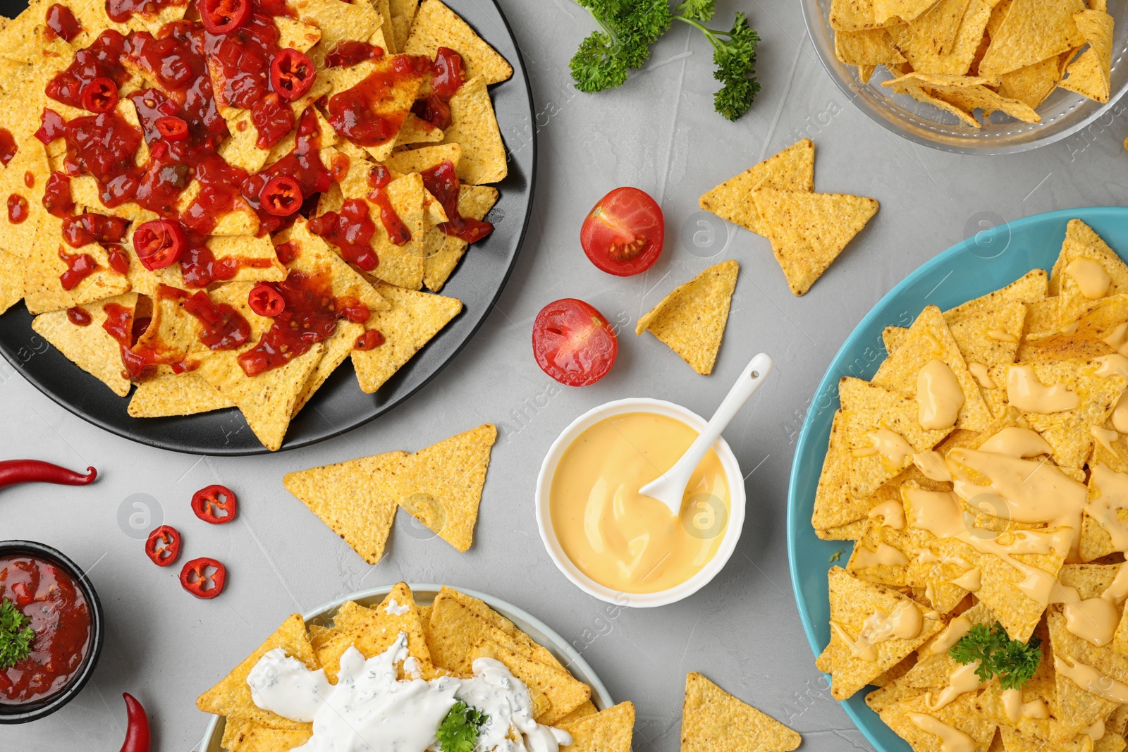 Photo of Mexican nacho chips with different sauces on grey table, flat lay