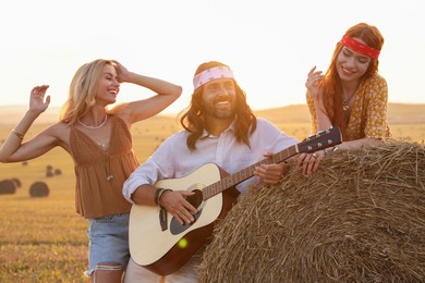 Beautiful hippie women listening to their friend playing guitar in field