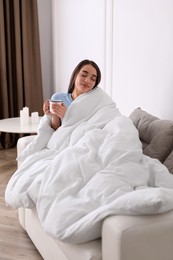 Photo of Woman covered in blanket holding cup of drink on sofa