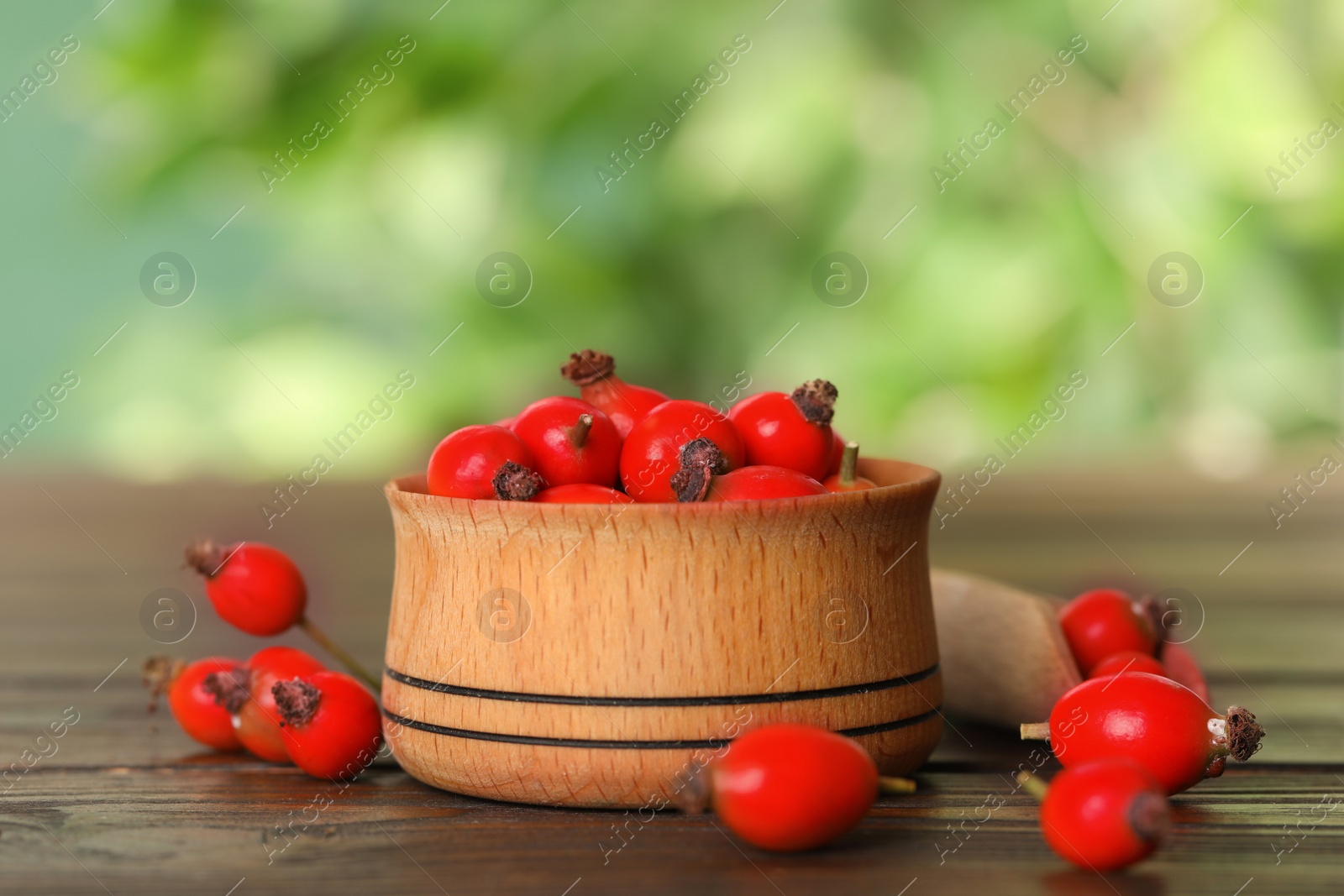 Photo of Ripe rose hip berries with bowl on wooden table