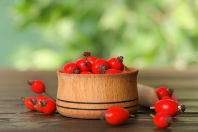 Photo of Ripe rose hip berries with bowl on wooden table