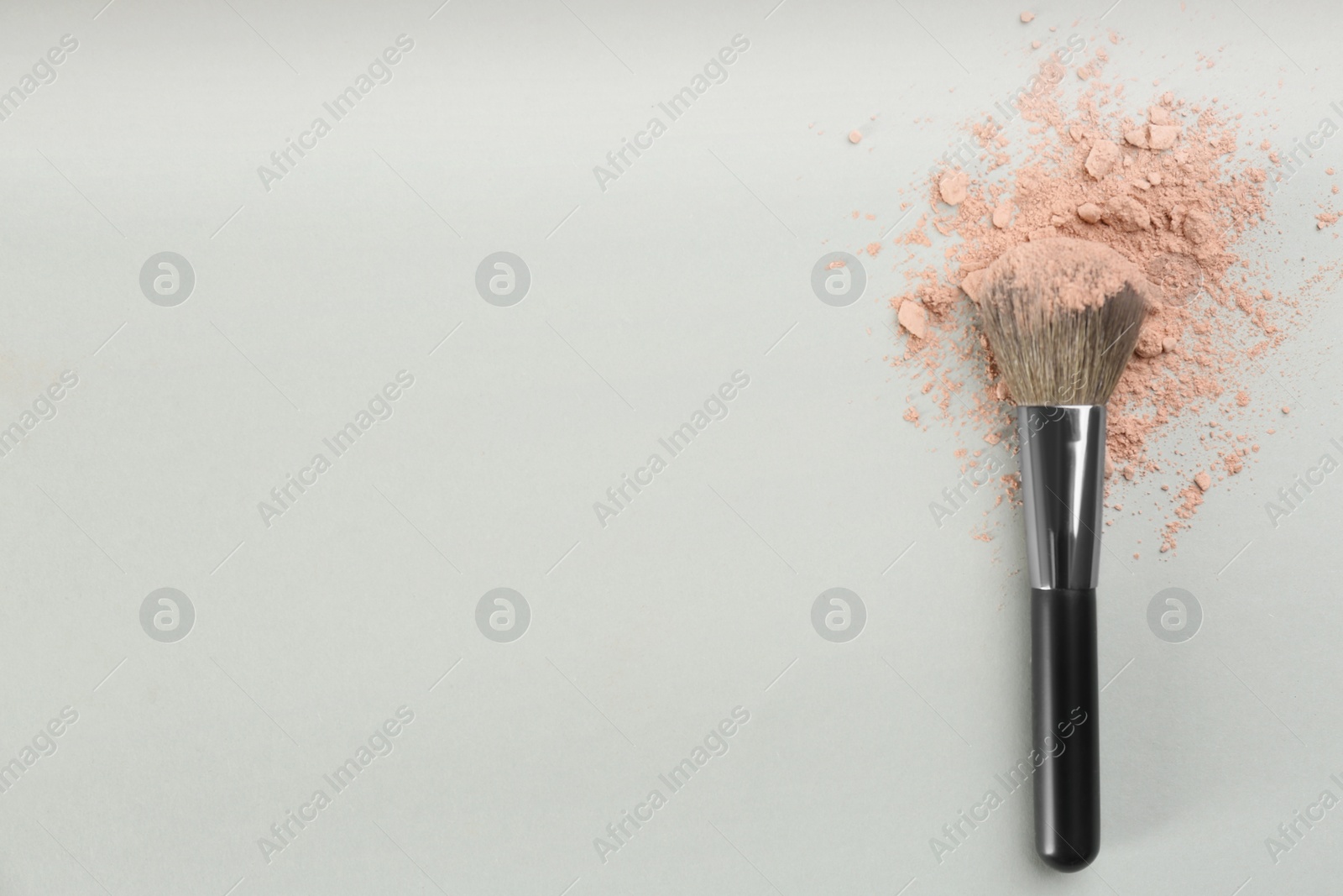 Photo of Makeup brush and scattered face powder on light grey background, top view. Space for text