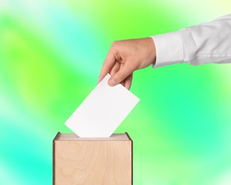 Man putting his vote into ballot box on color background, closeup