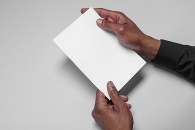 Photo of African American man holding sheet of paper on white background, closeup. Mockup for design