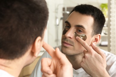 Photo of Young man applying under eye patches near mirror at home