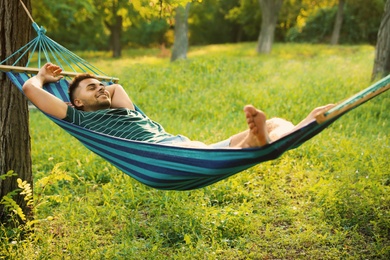 Young man resting in comfortable hammock at green garden