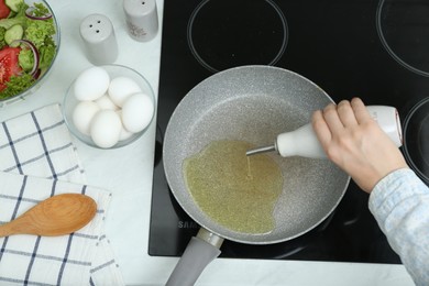 Photo of Woman pouring cooking oil from bottle into frying pan in kitchen, top view