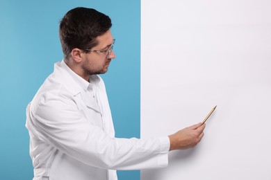 Photo of Ophthalmologist pointing at blank banner on light blue background, space for text