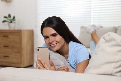 Happy young woman having video chat via smartphone on sofa in living room