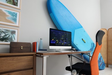 Photo of Stylish workplace with modern computer and SUP board near light wall in room. Interior design