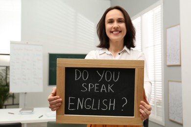 Photo of Teacher holding small chalkboard with inscription Do You Speak English? in classroom
