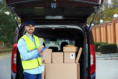 Photo of Young courier checking amount of parcels in delivery van, outdoors