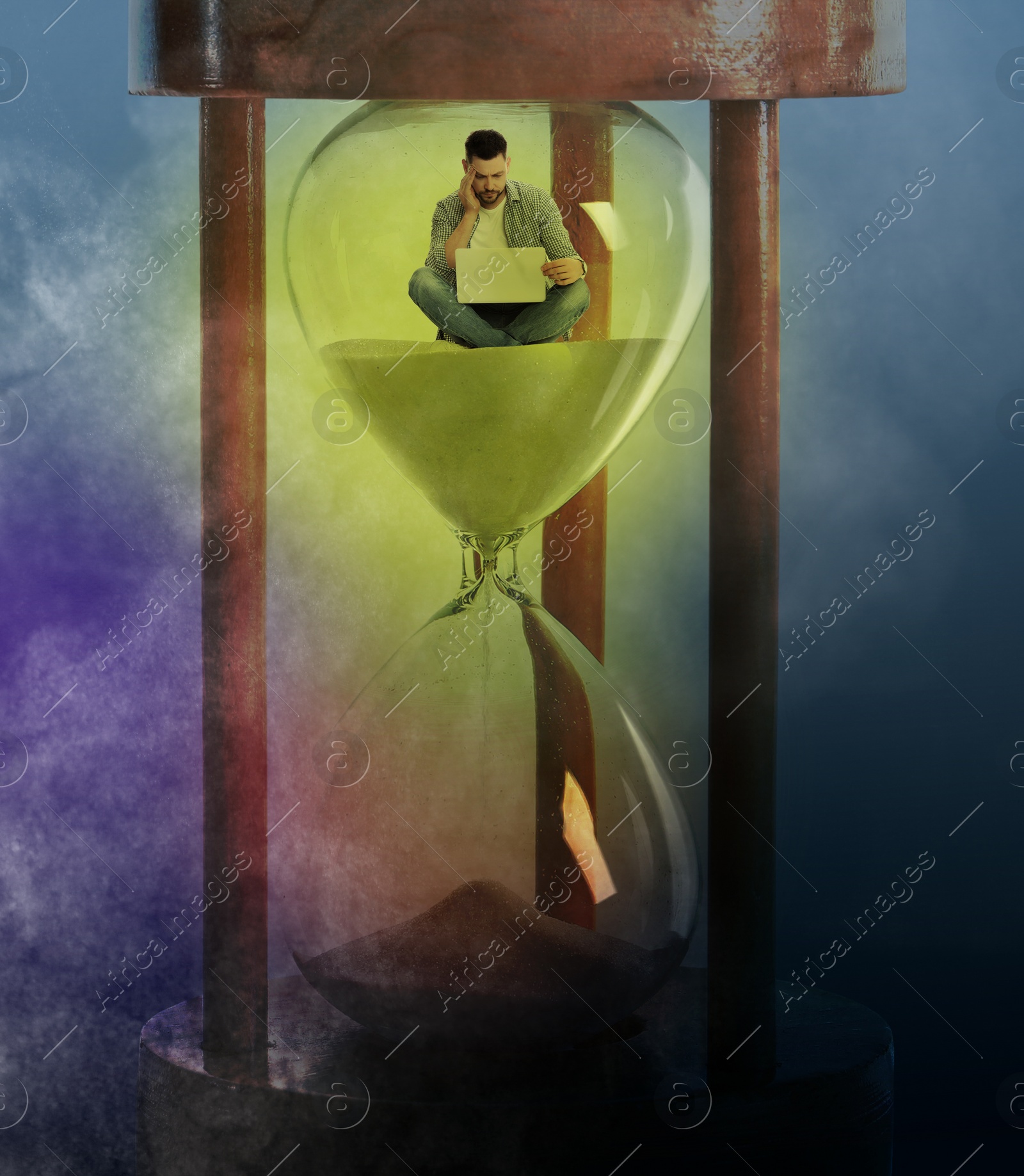 Image of Man with laptop sitting inside hourglass on color background. Flowing sand symbolizing coming deadline