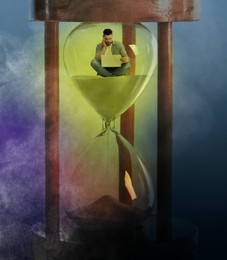 Man with laptop sitting inside hourglass on color background. Flowing sand symbolizing coming deadline