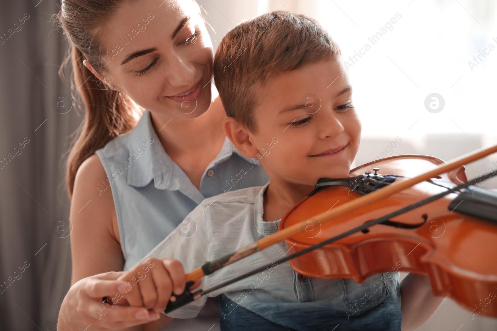 Photo of Young woman teaching little boy to play violin indoors