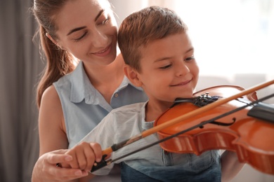 Photo of Young woman teaching little boy to play violin indoors