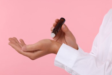 Photo of Woman with roller bottle applying essential oil onto wrist on pink background, closeup