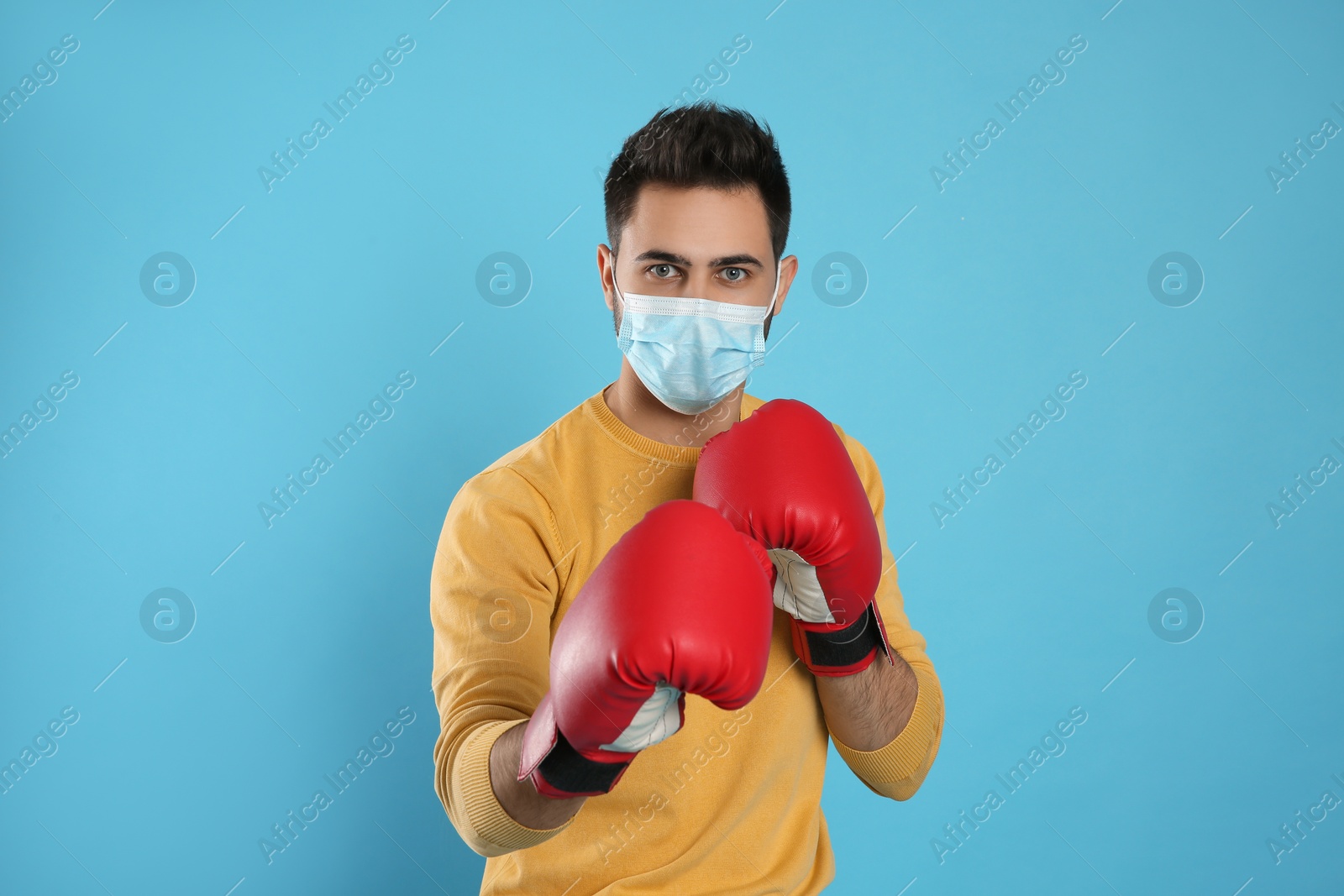 Photo of Man with protective mask and boxing gloves on light blue background. Strong immunity concept