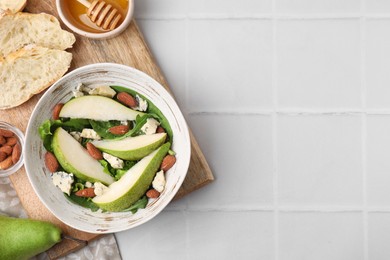 Photo of Delicious pear salad in bowl and products on light tiled table, top view. Space for text