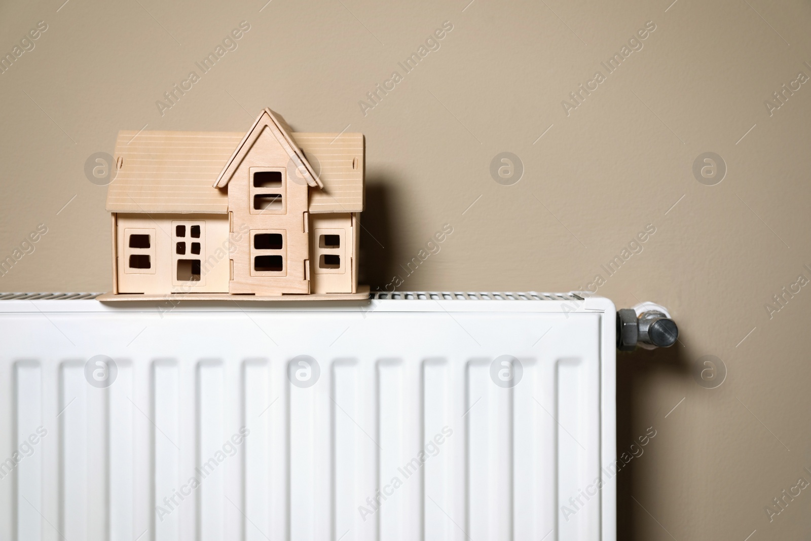 Photo of Modern radiator with wooden house near beige wall indoors. Winter heating efficiency