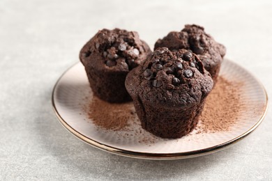 Delicious chocolate muffins and cacao powder on light grey table. Space for text