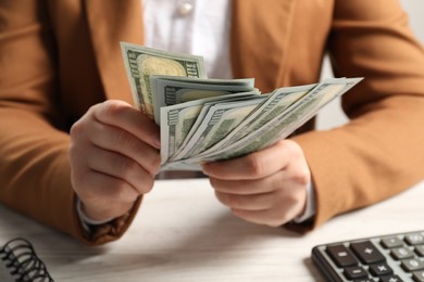 Photo of Money exchange. Woman holding dollar banknotes at white wooden table, closeup